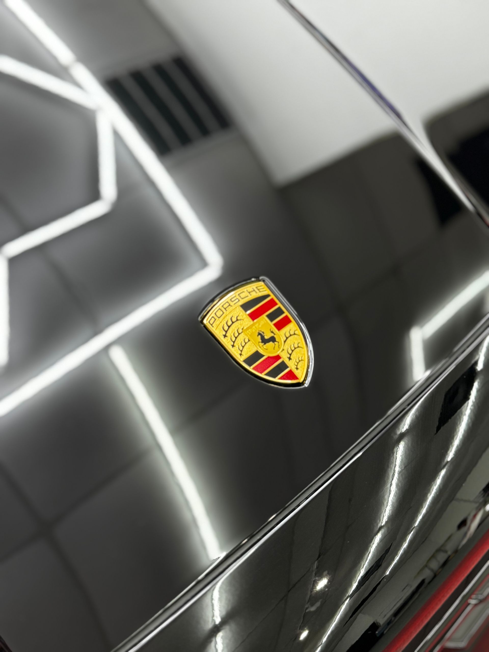 Close-up of a glossy black Porsche hood with the Porsche crest under bright showroom lights