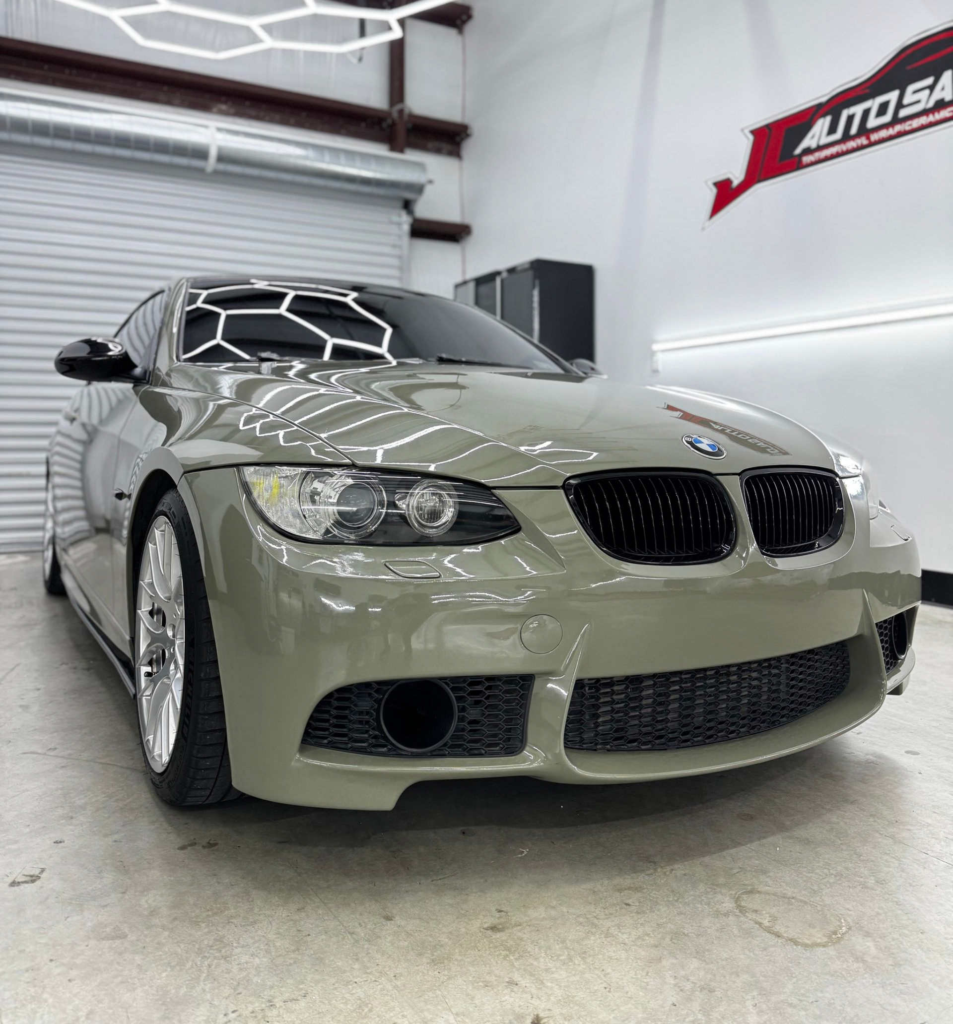 Customized beige BMW coupe in a bright auto shop, front view with lowered stance and wide body kit