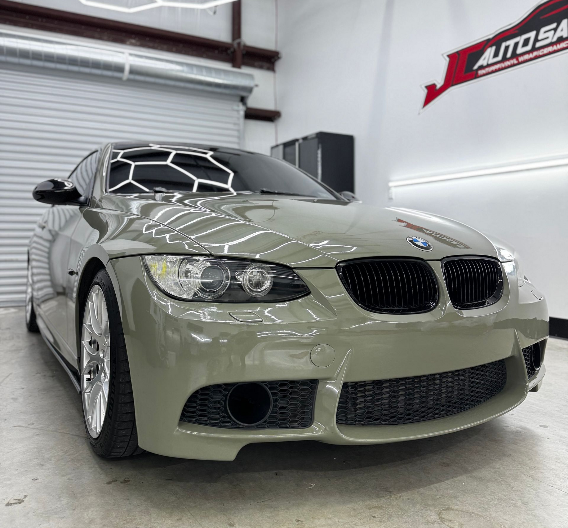 Gray BMW coupe in a showroom with a black geometric roof wrap and AUTOSA sign on the wall