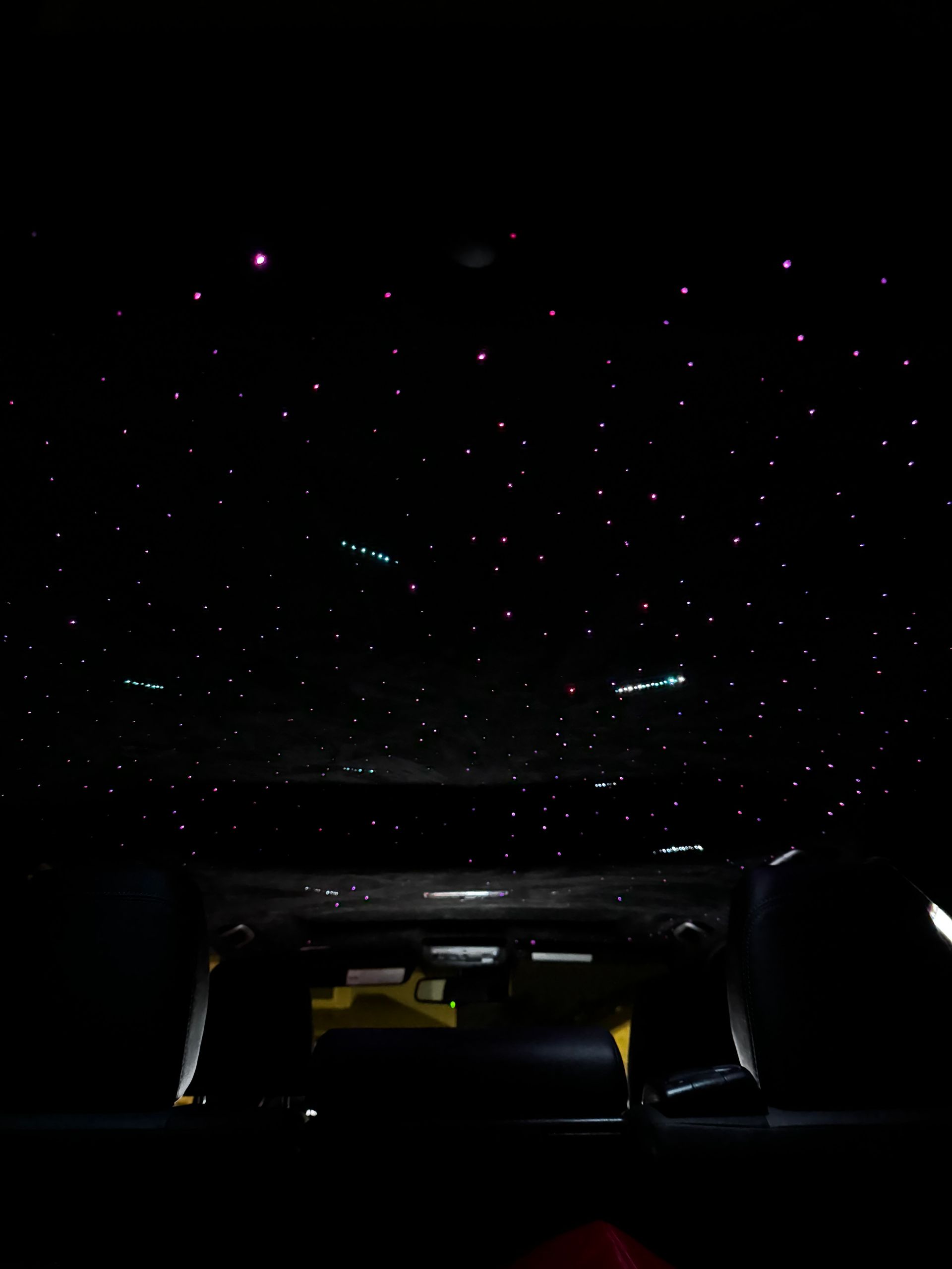 Dark car interior beneath a starry ceiling with faint glowing lights and dashboard glow