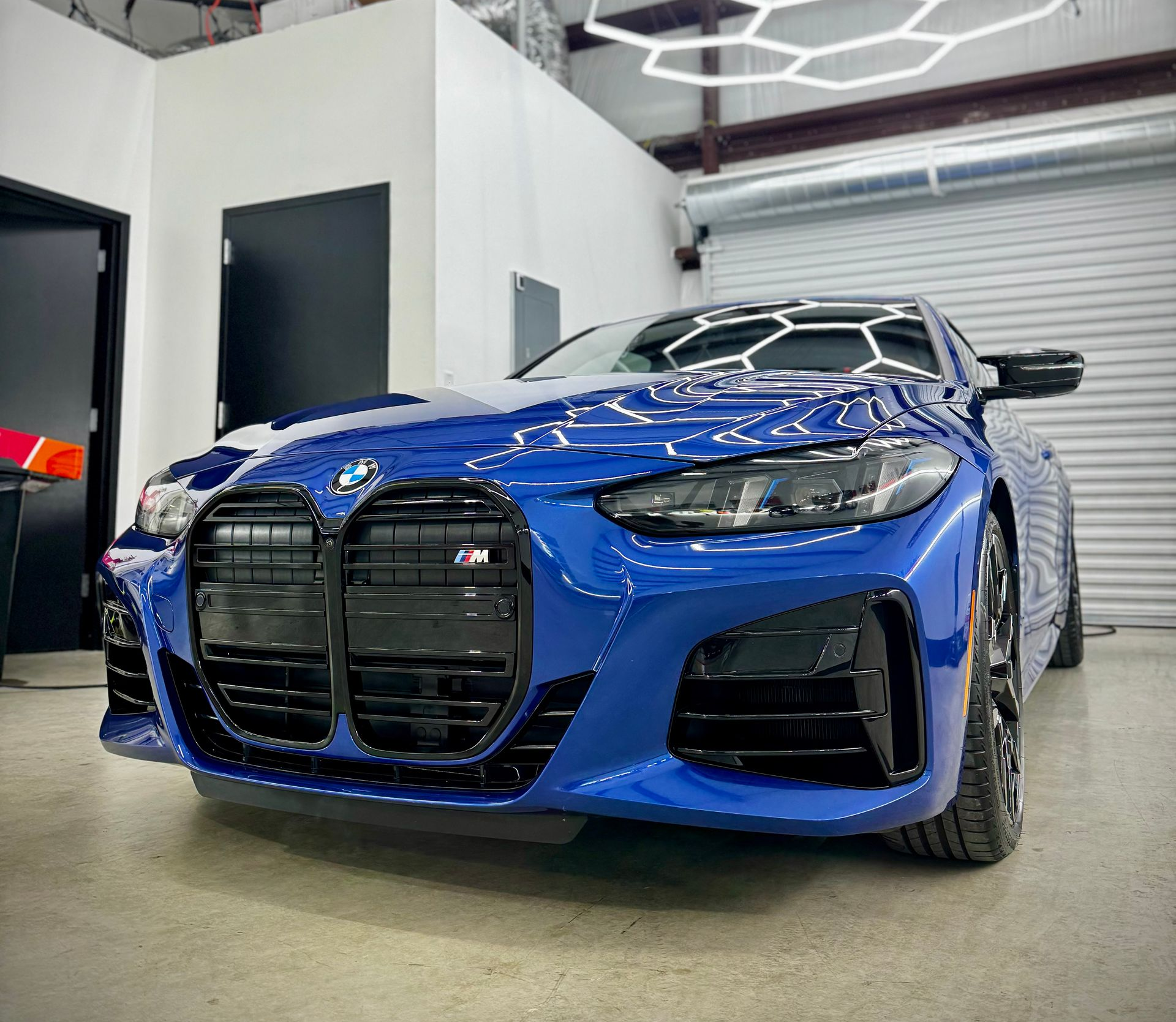 Close-up of a gray car’s front grille and headlight in an auto shop with color sample boards in the background