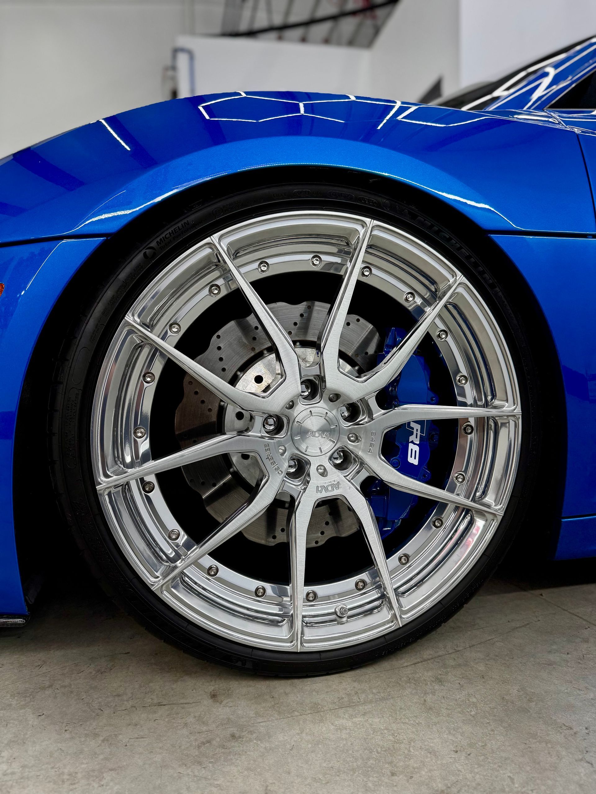 Close-up of a blue sports car’s chrome wheel and low-profile tire in a garage