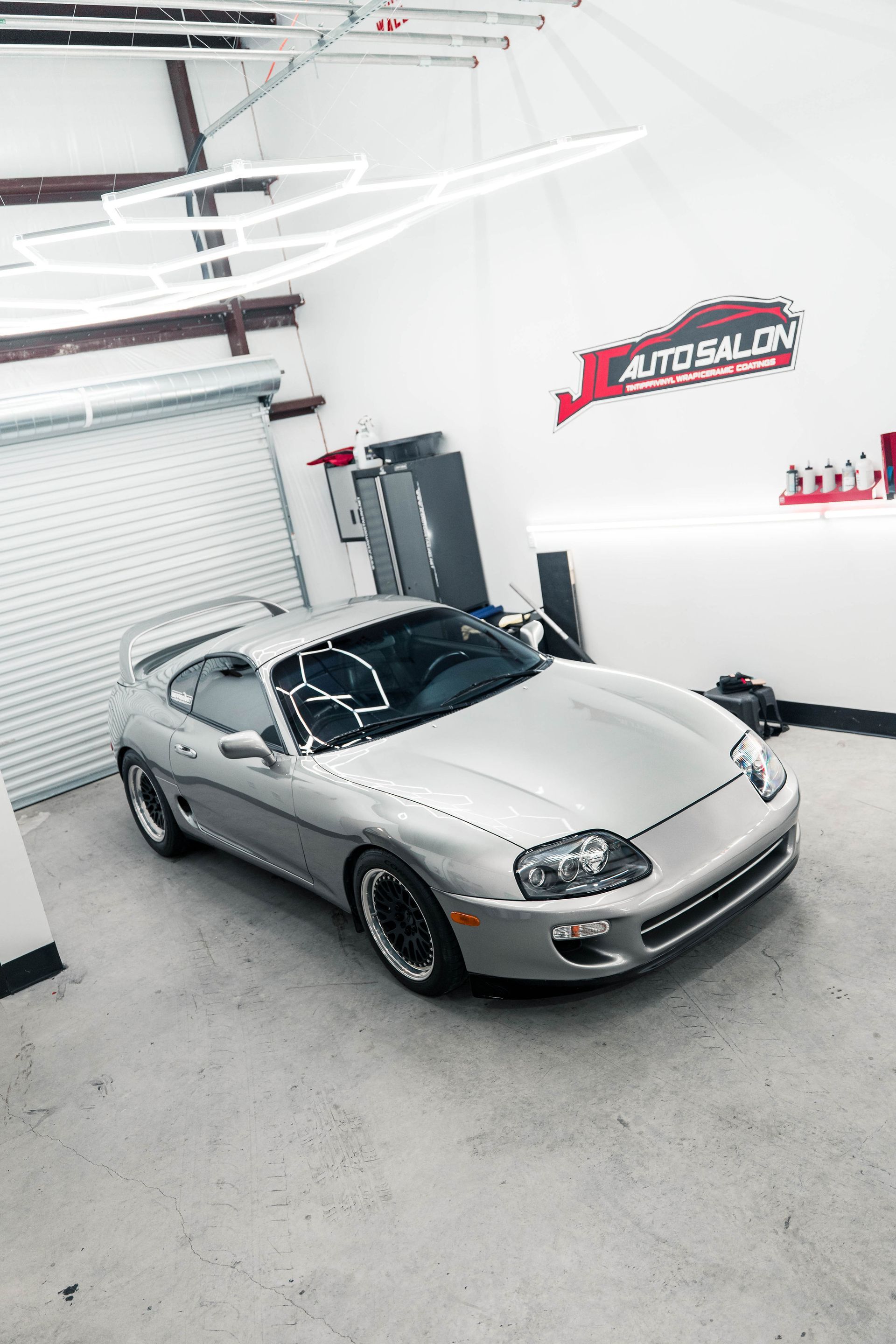 Silver sports car in a bright garage with white walls and overhead lights