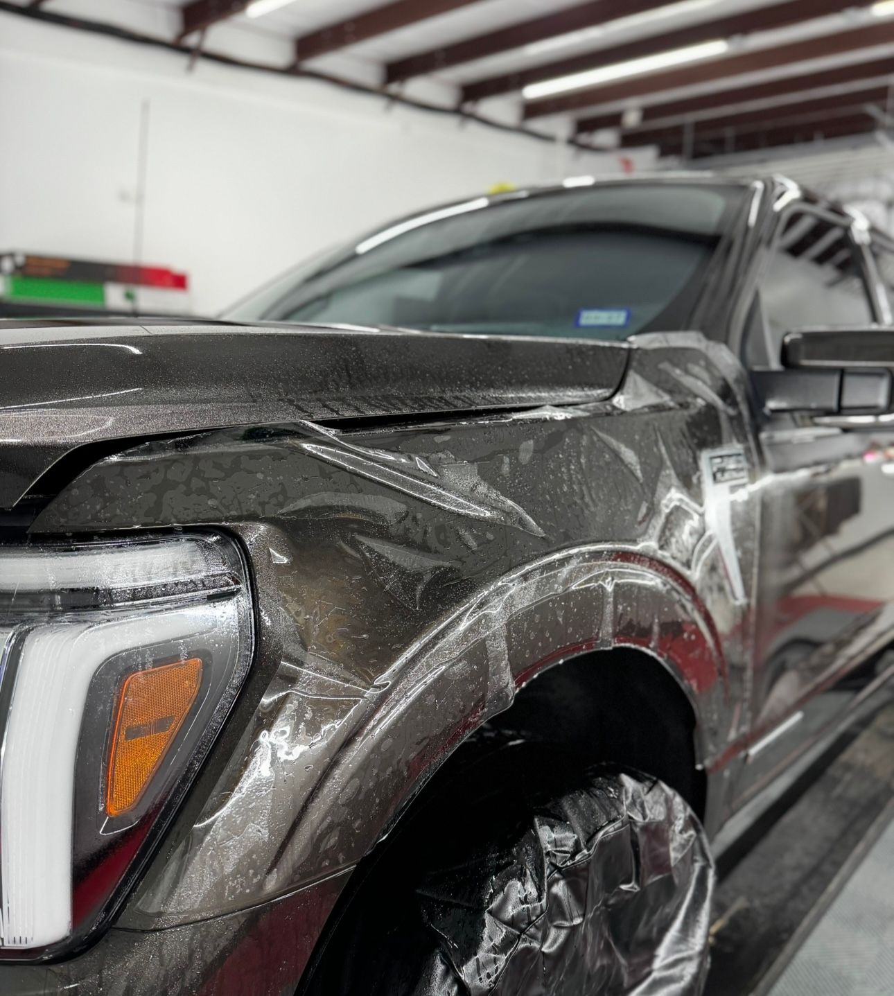 Damaged black pickup truck in a garage, with wrinkled fender and covered wheel