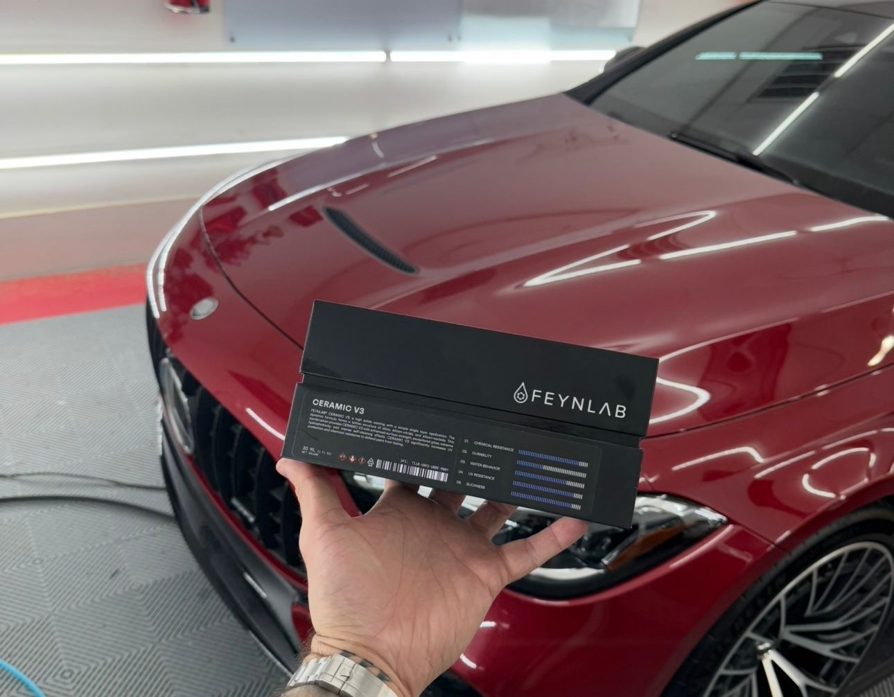Hand holding a black card in front of a red car’s front grille in a showroom