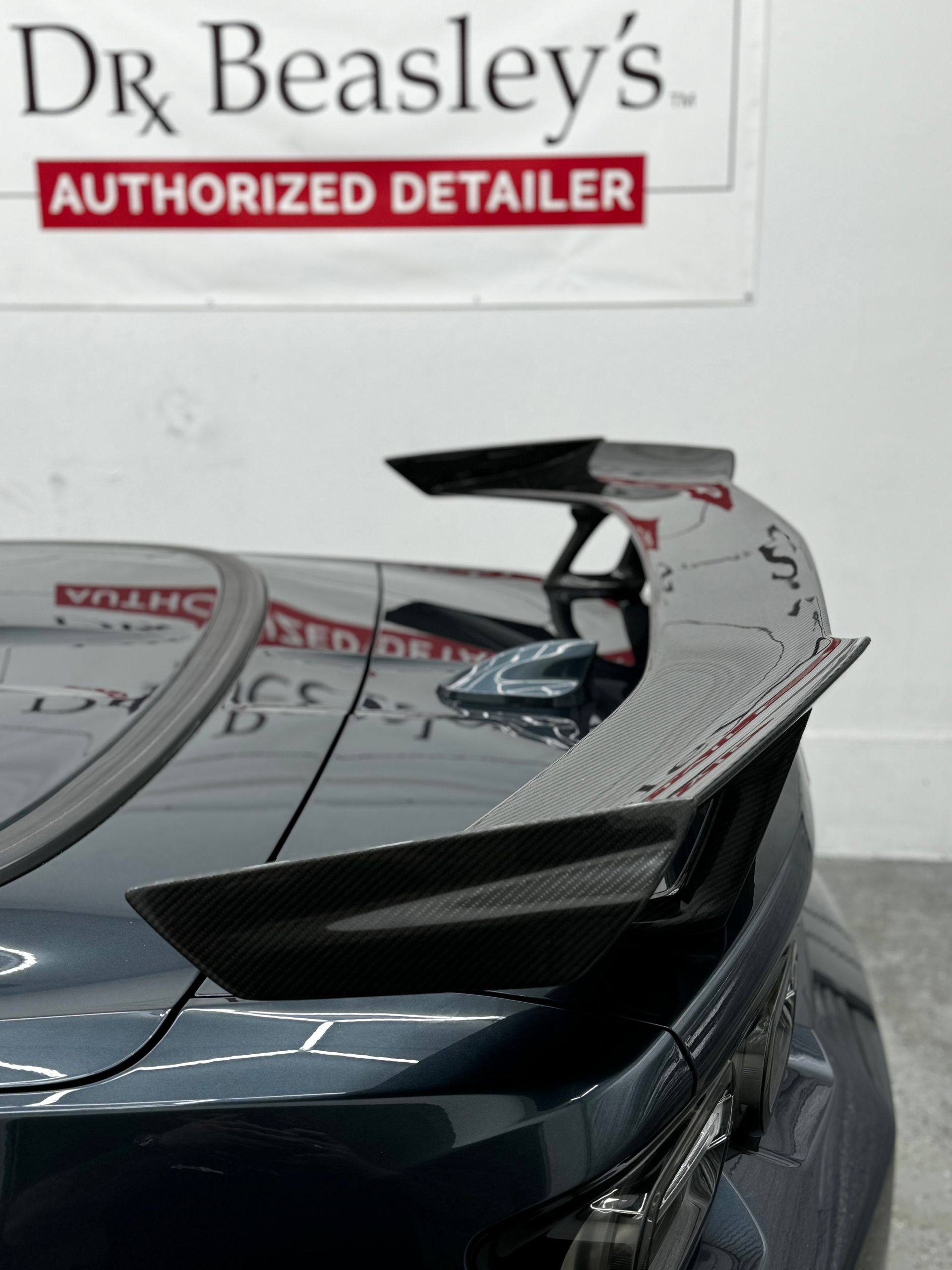 Close-up of a gray car’s front grille and headlight in an auto shop with color sample boards in the background