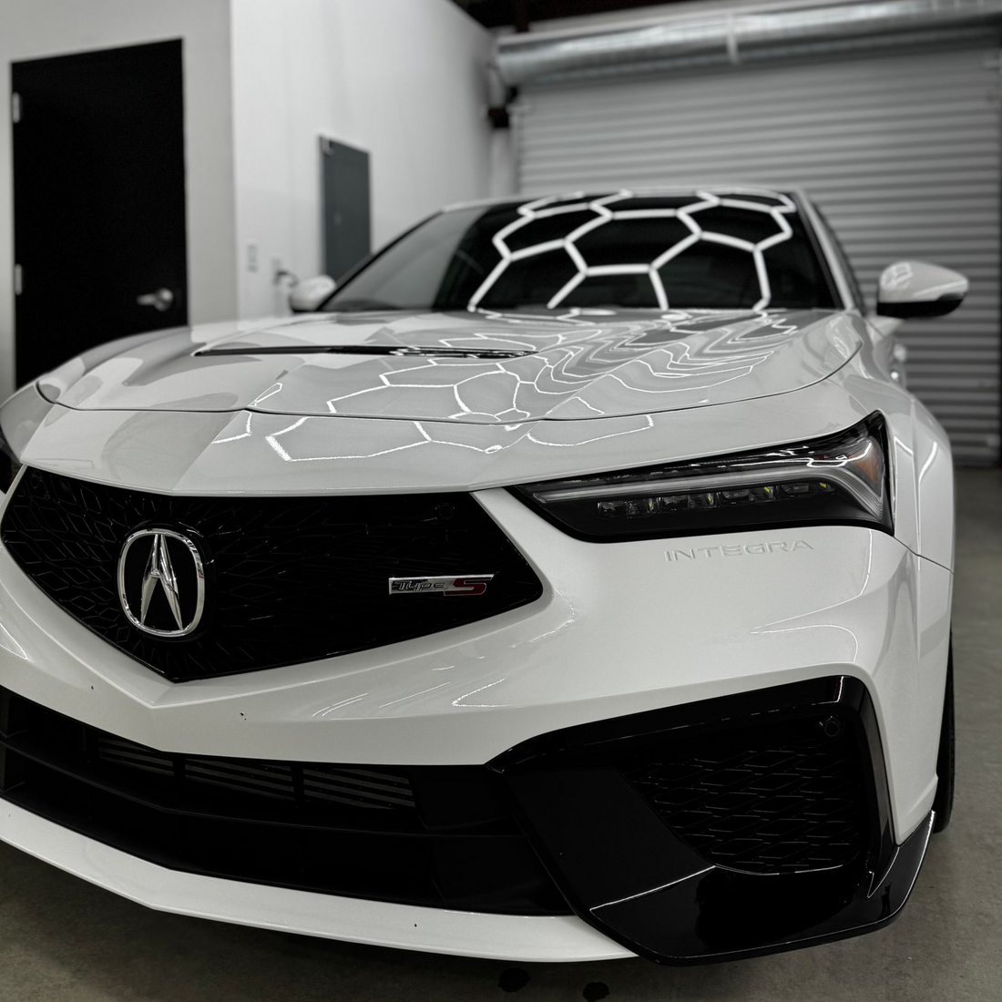 White Acura sports sedan in a garage, front view with a patterned windshield wrap