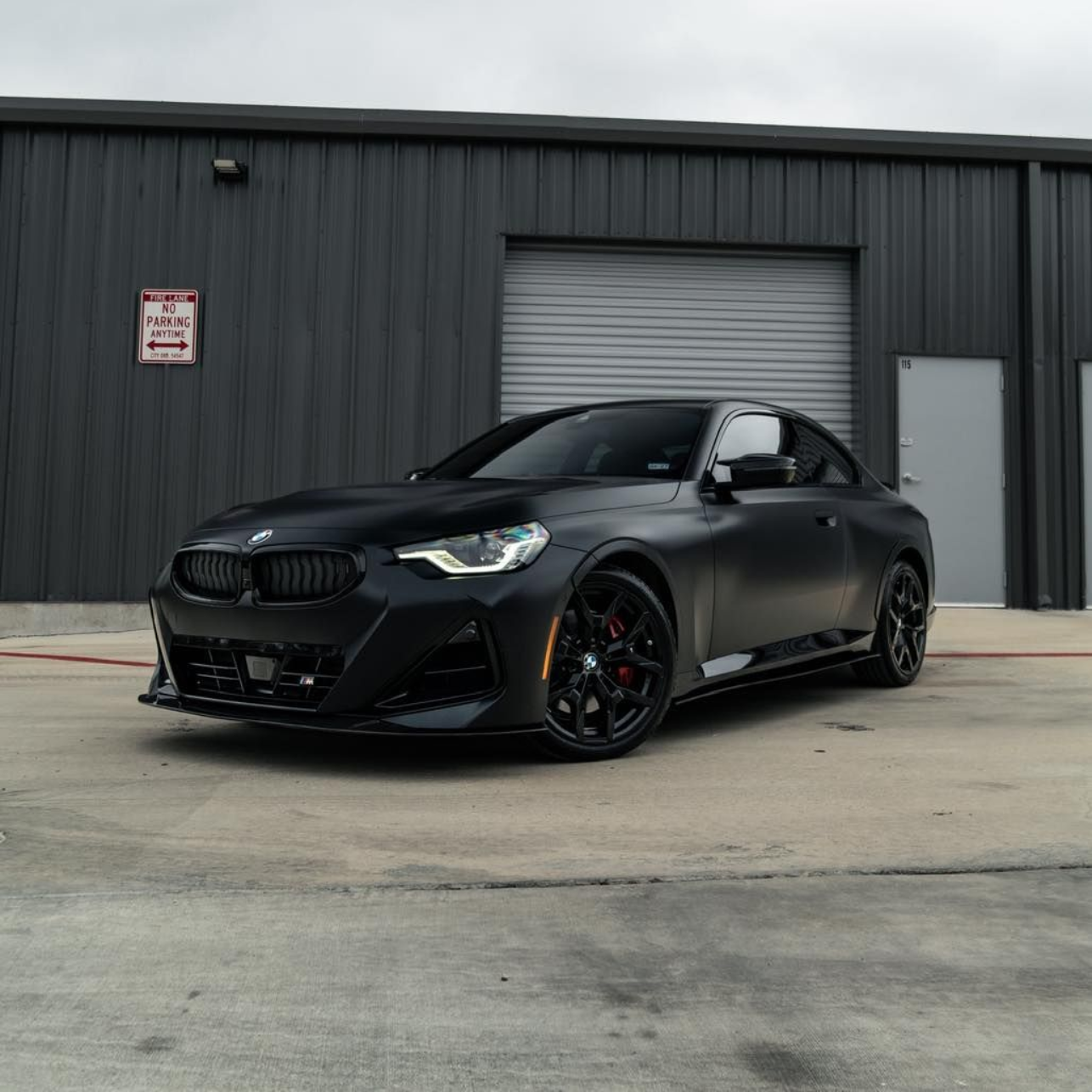 Black sports coupe parked in front of a gray industrial building and garage door