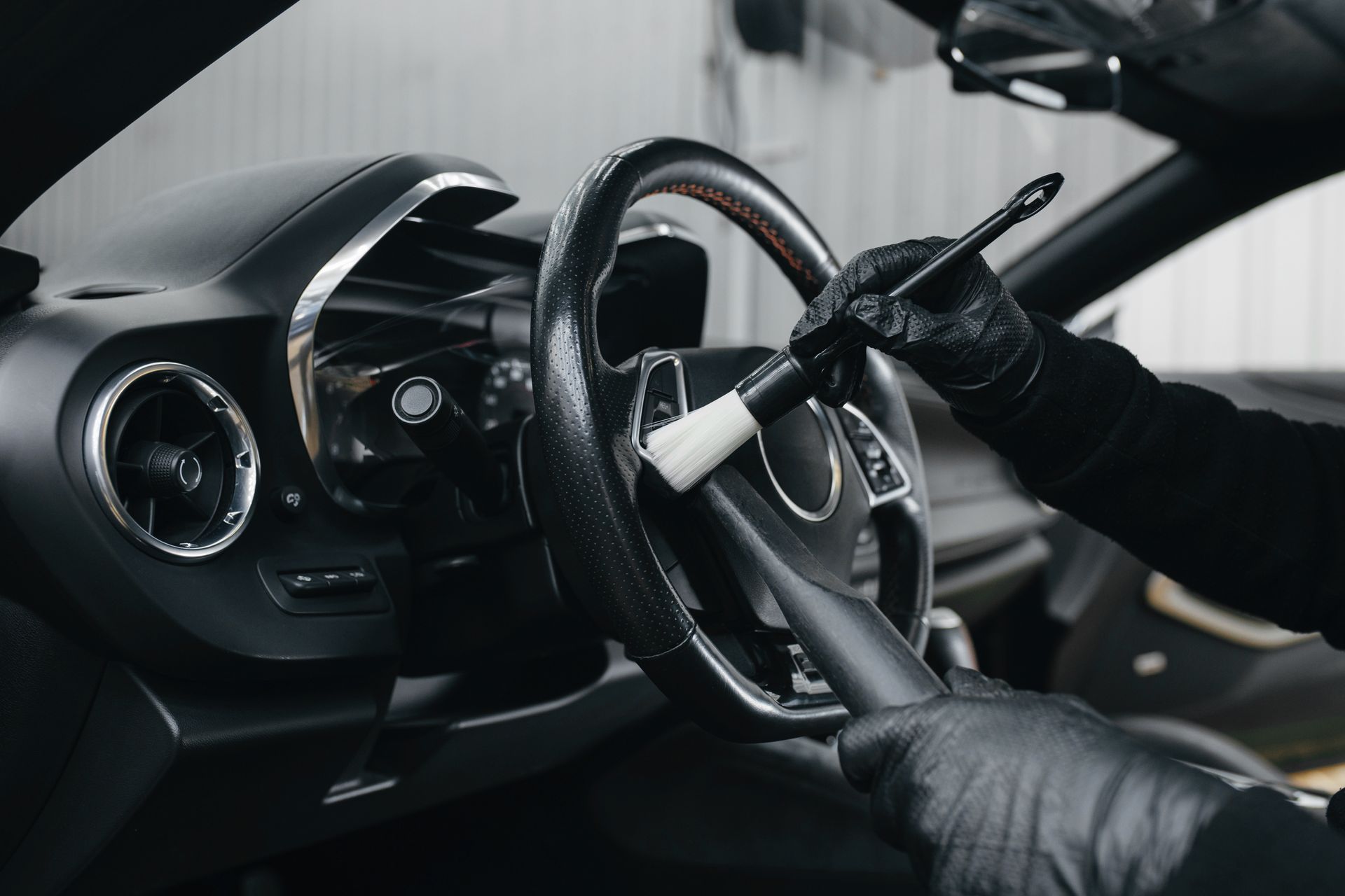 Gloved hands gripping a car steering wheel inside a dark, modern vehicle interior