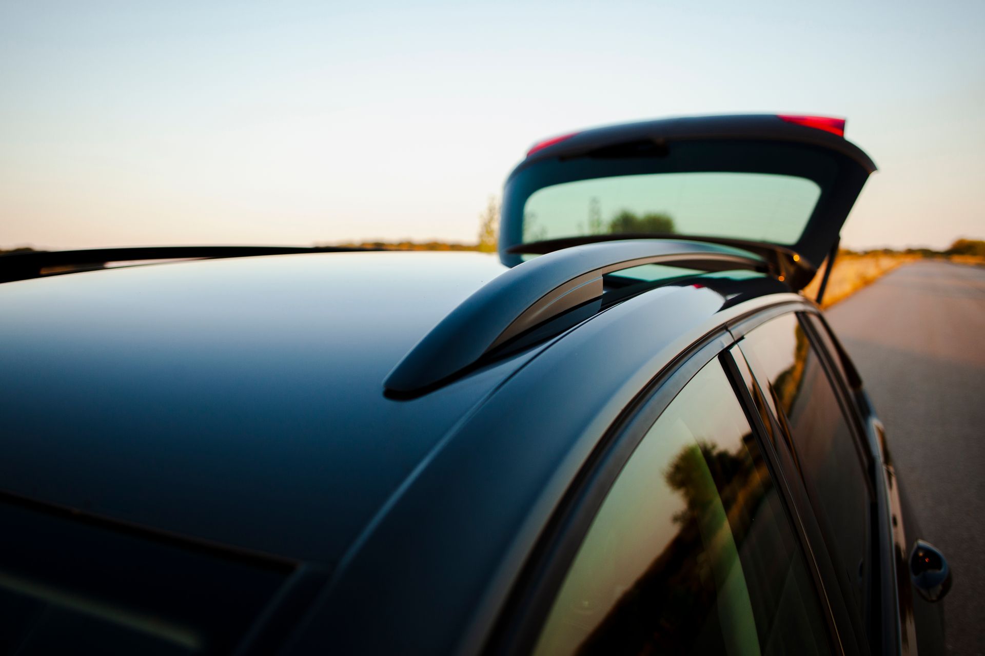 Black car driving on a road at sunset, rear hatch open with a roof spoiler visible