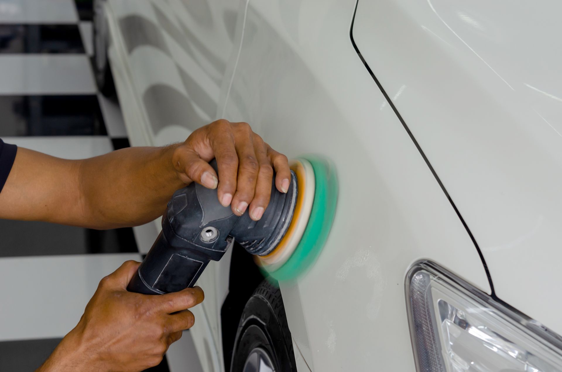 Person polishing a white car with a handheld buffer in a garage