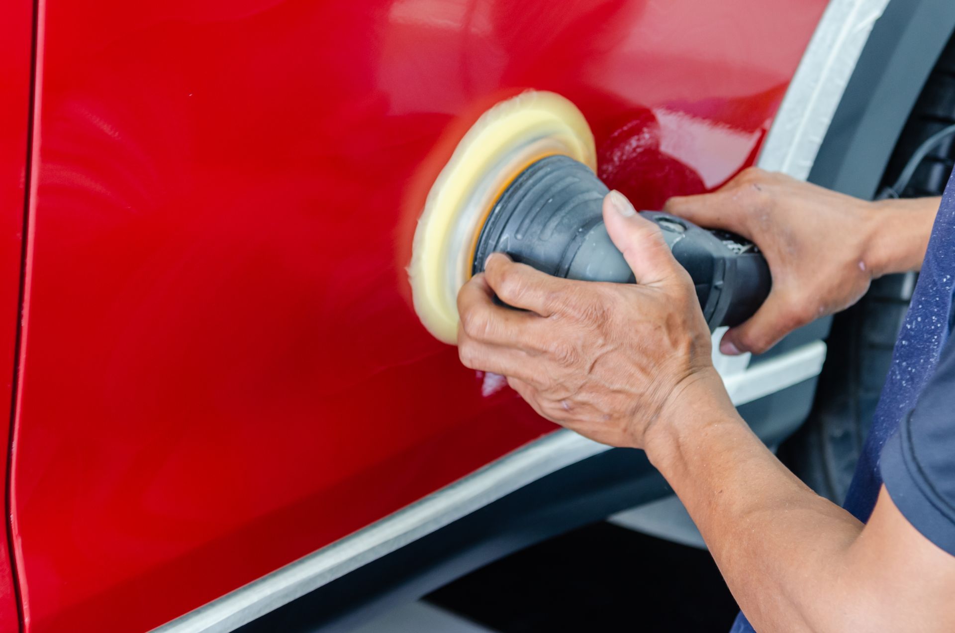 Hands polishing a red car door with a buffer