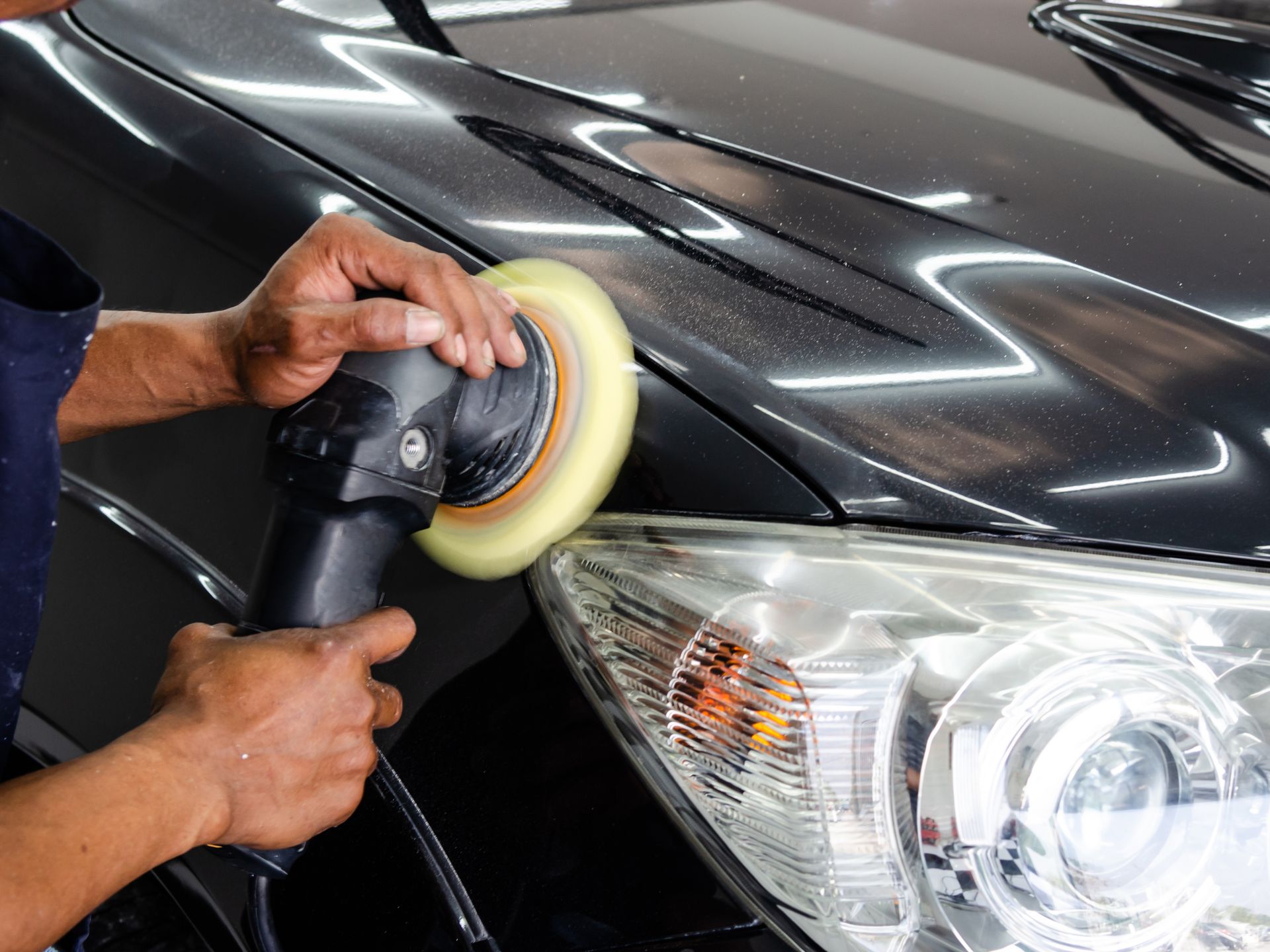 Hands polishing a black car’s headlight with a buffer tool