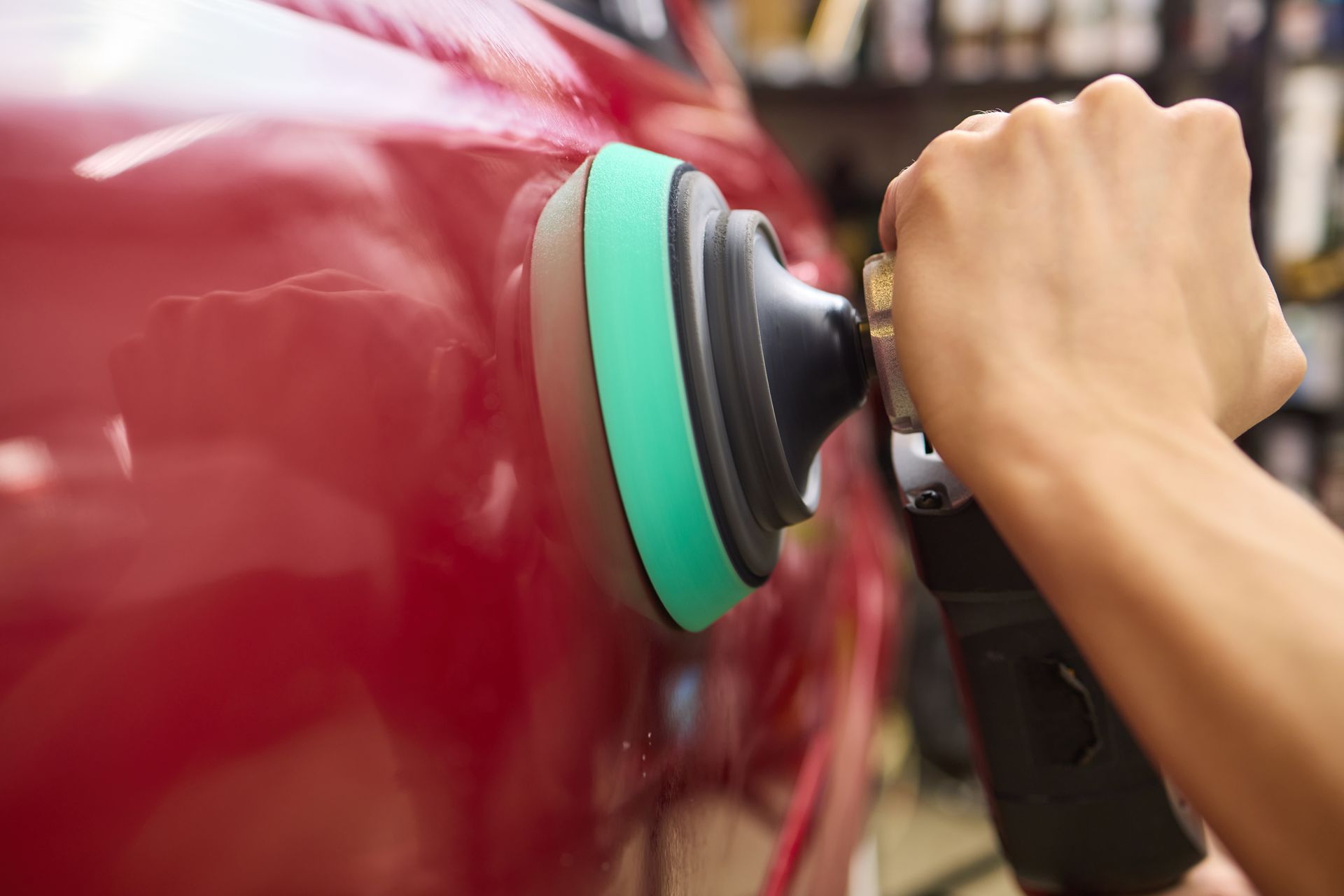 Hand polishing a red car with a rotary buffer and green pad