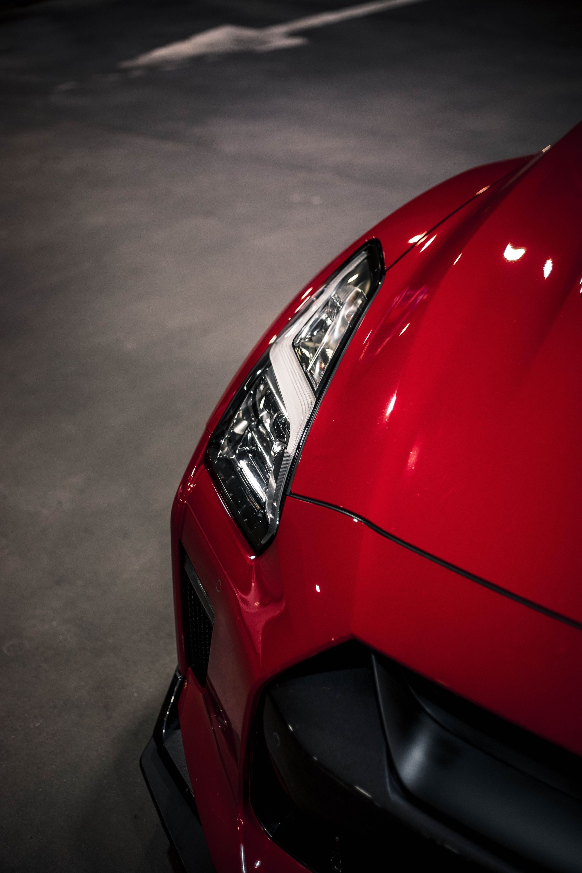 Close-up of a red sports car’s front corner and headlight in a dim garage