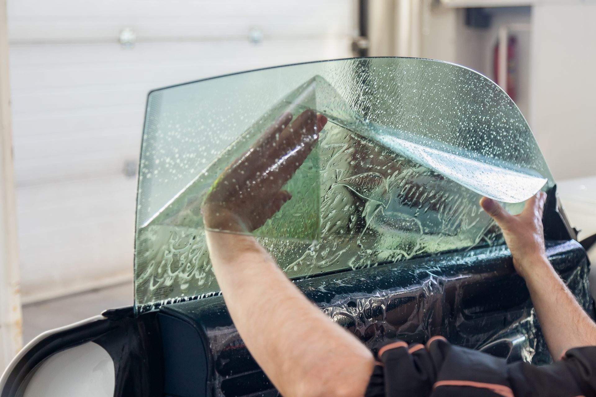 Hands peeling a large clear plastic sheet from a black chair outdoors