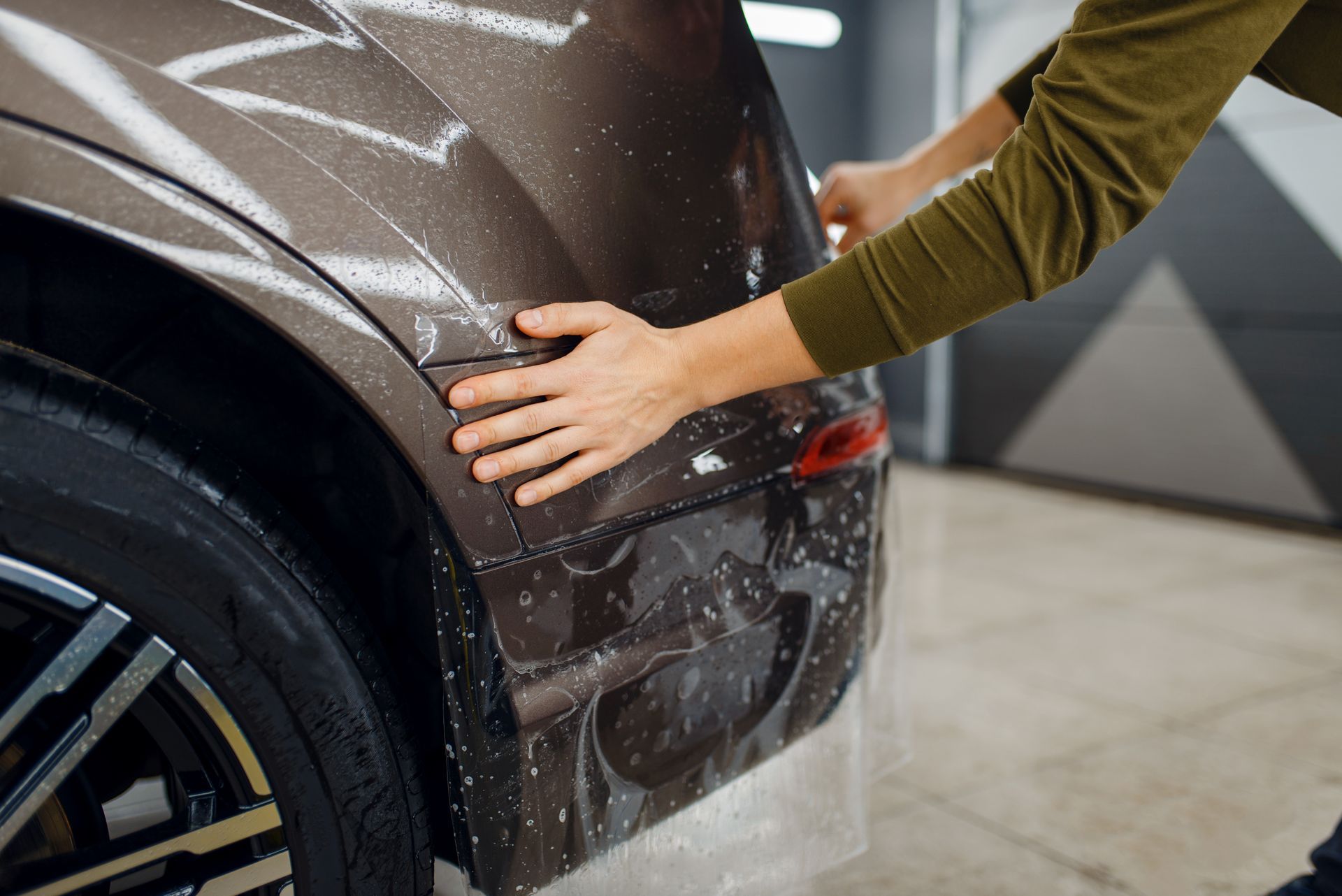 Person wiping a brown car’s rear panel in a garage