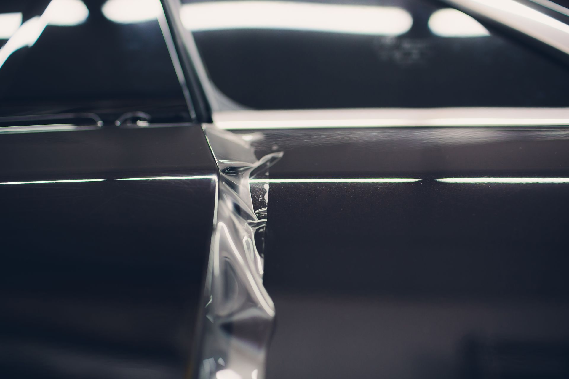 Close-up of two glossy black car panels separated by a crumpled silver seam
