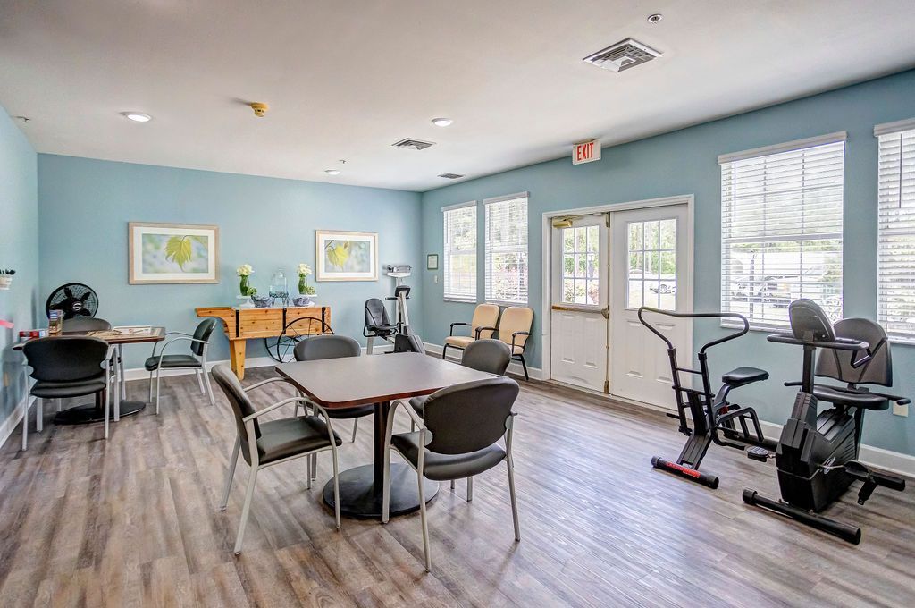 Bright common room with tables, chairs, and exercise bikes by windows