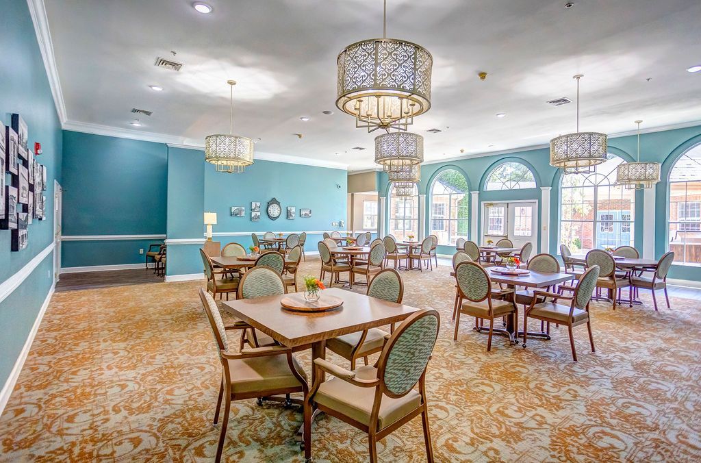 Bright dining room with blue walls, patterned carpet, tables, and wicker chairs by large windows