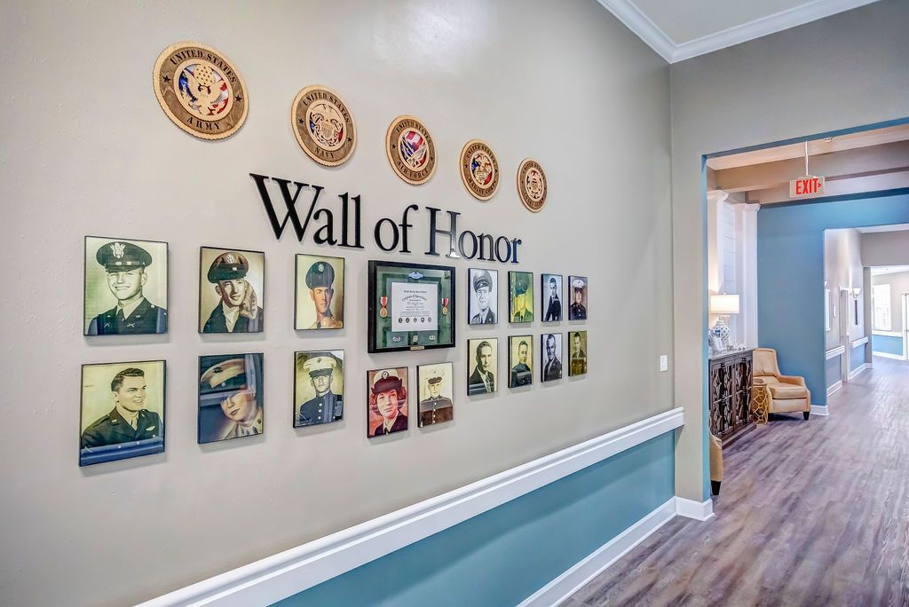 Wall of Honor with framed portraits in a hallway, with a doorway and chairs in the background