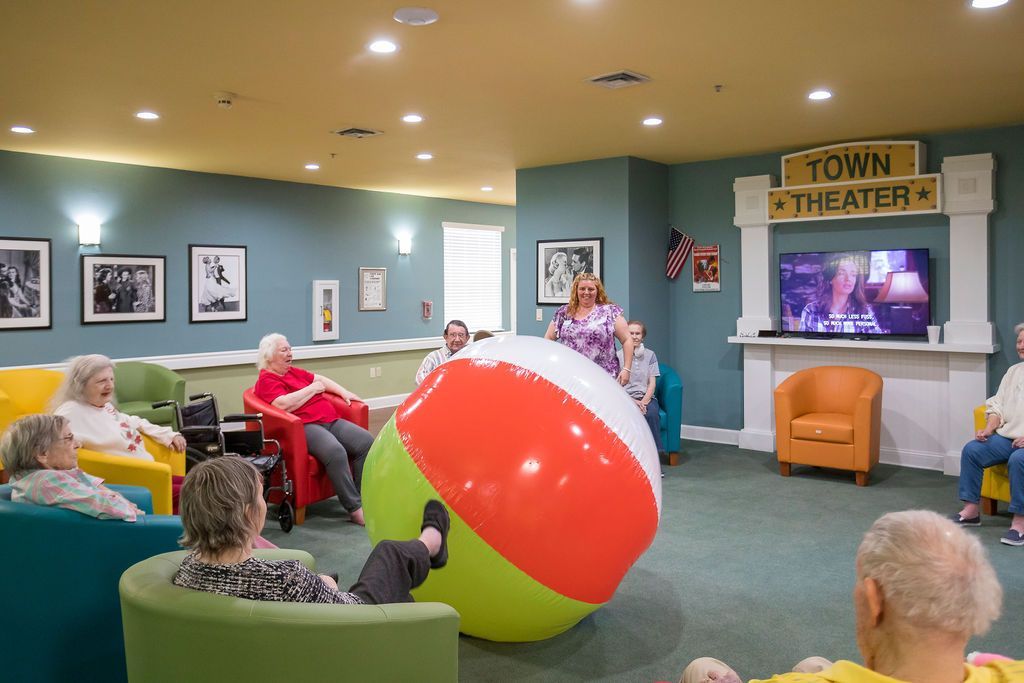 People in a lounge watching TV, with a giant red-and-yellow beach ball in the center