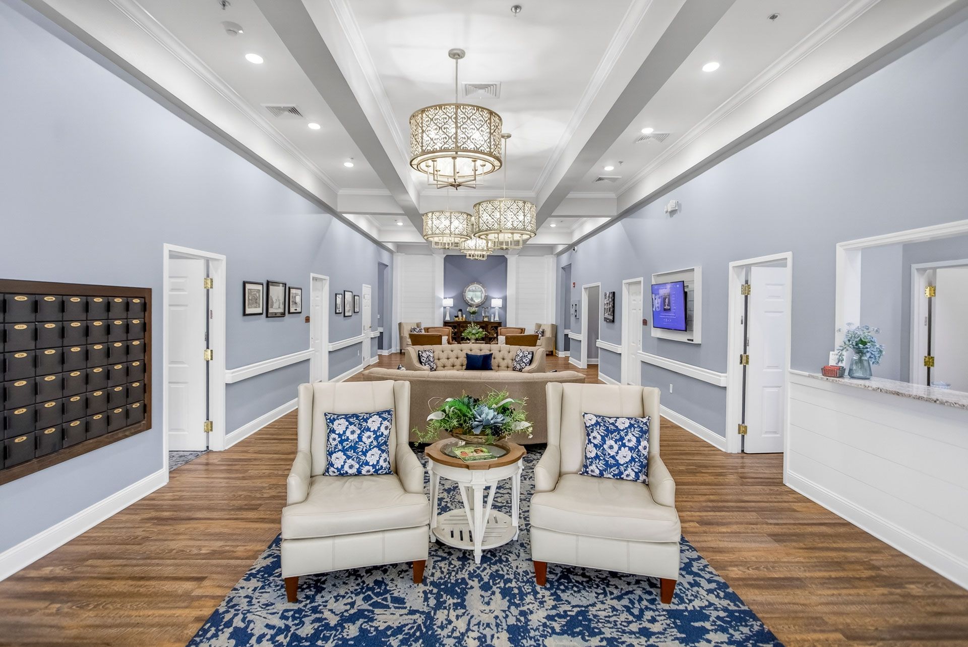 Bright, elegant lobby with cream chairs, blue rug, chandeliers, mailboxes, and a reception desk.