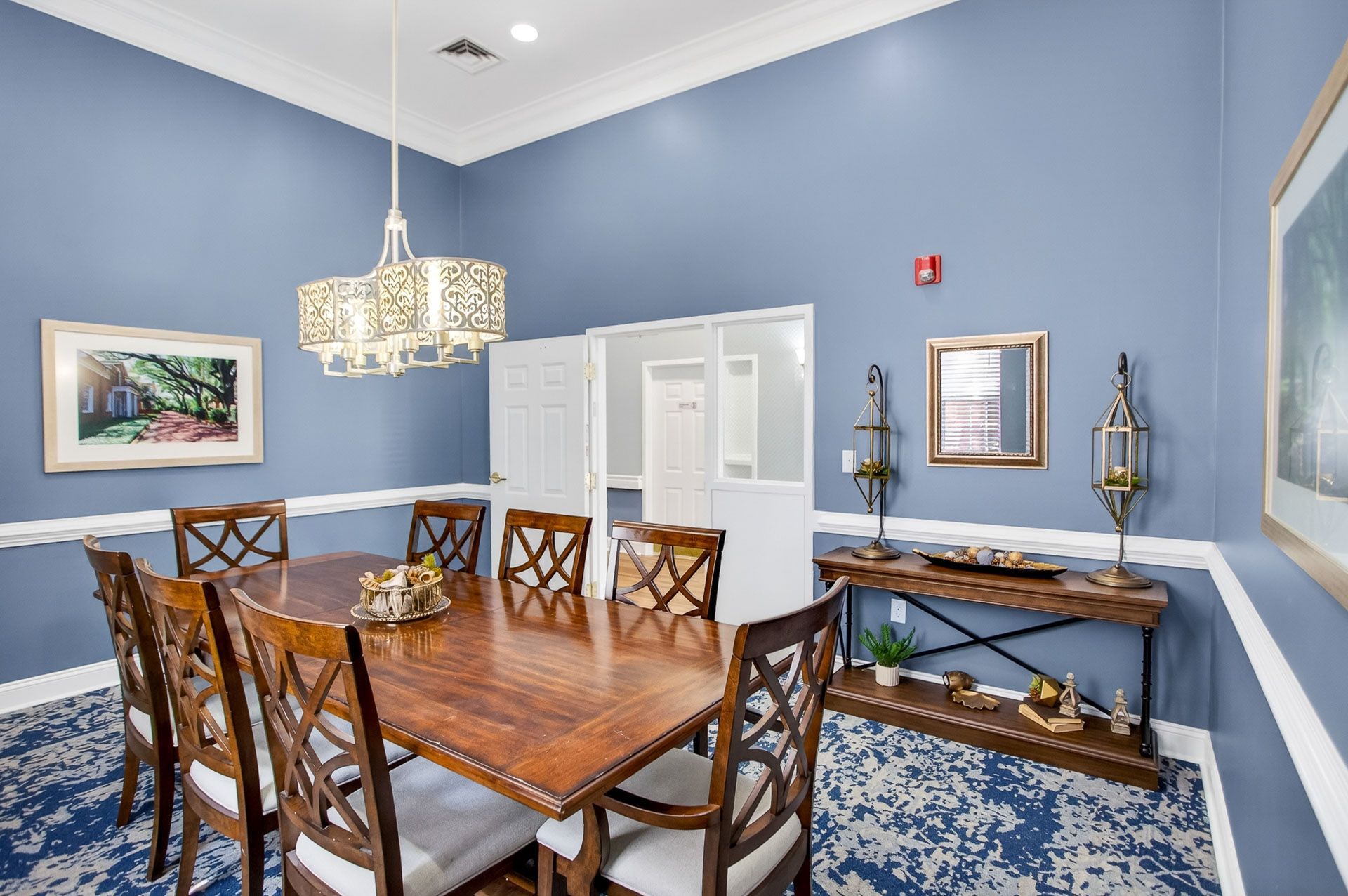 Elegant dining room with blue walls, wooden table and chairs, chandelier, and sideboard with decor