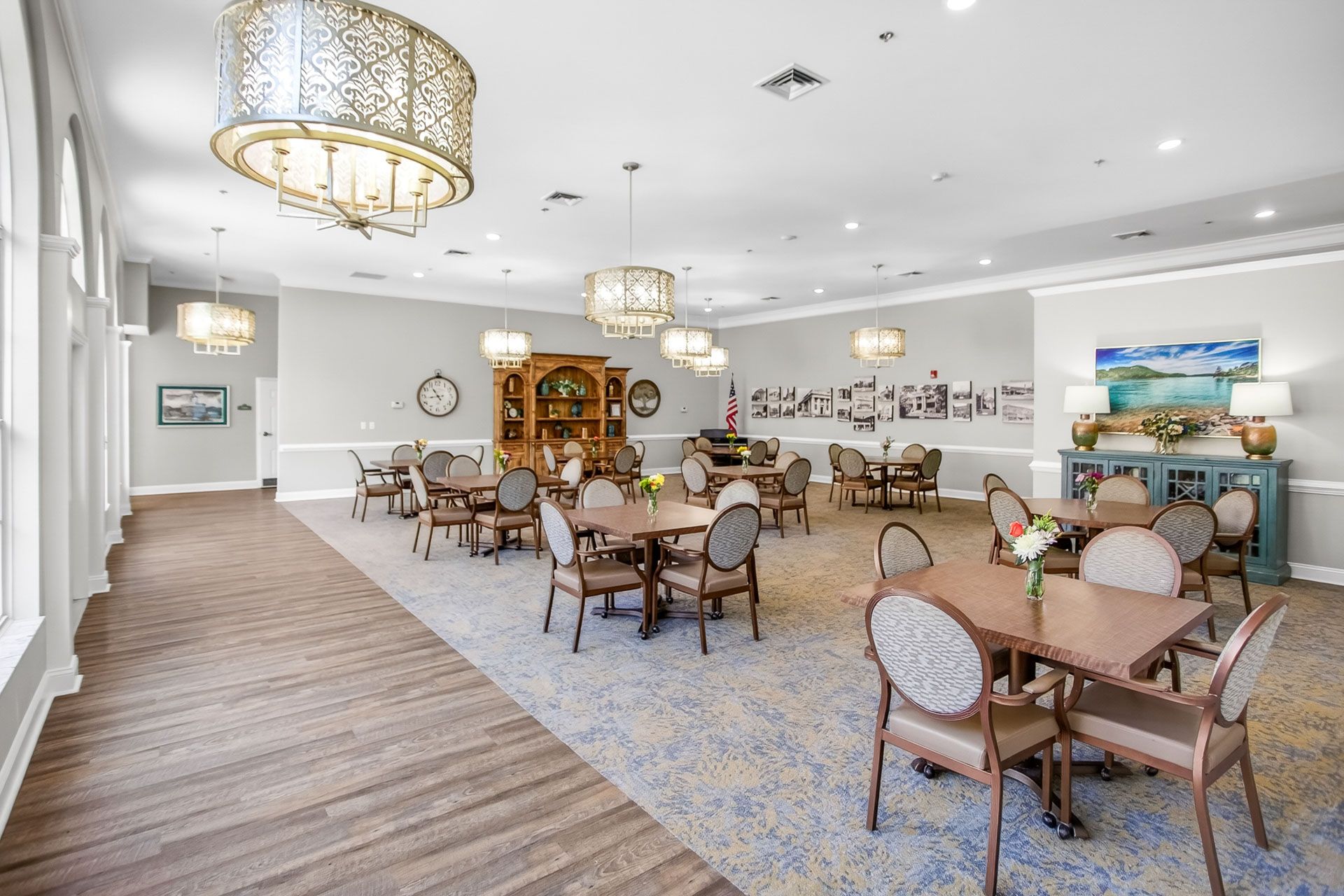 Spacious dining hall with round tables, chairs, chandeliers, and coastal artwork on the walls