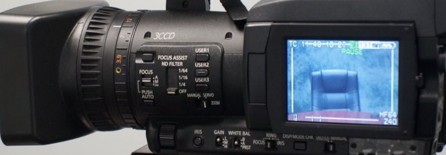 Close-up of a professional video camera with a screen displaying a blue chair in a studio setting.
