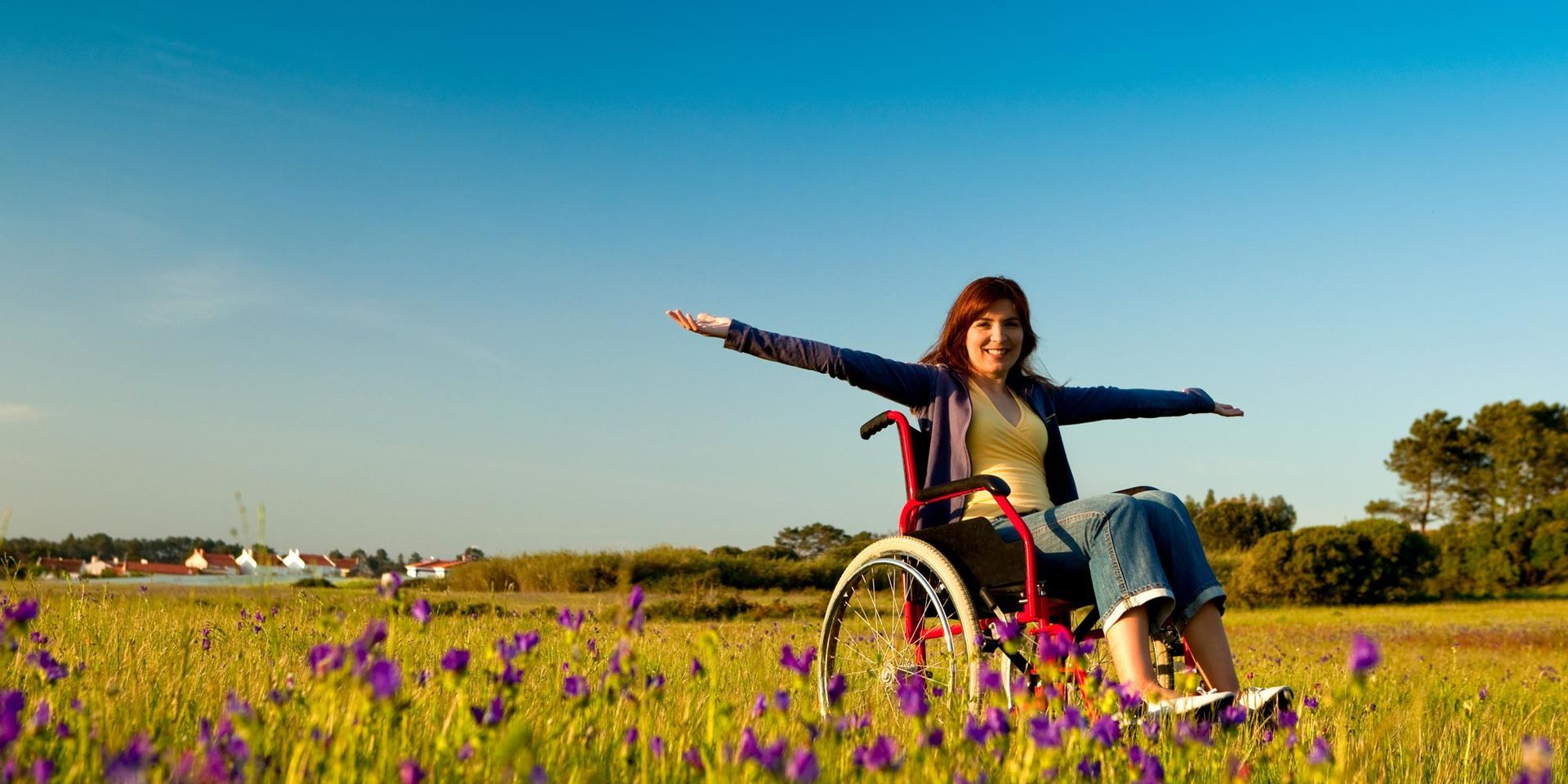A woman in a wheelchair is sitting in a field of flowers with her arms outstretched.