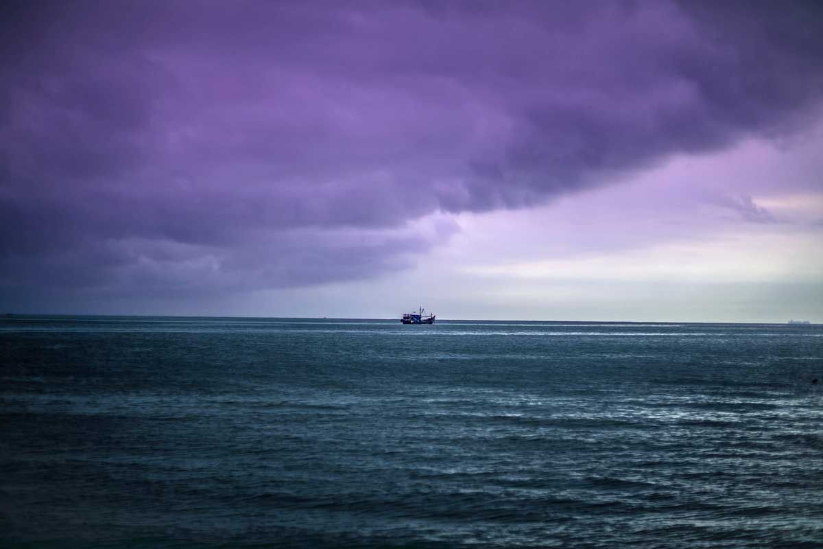 Purple storm clouds over a dark ocean with a small boat on the horizon