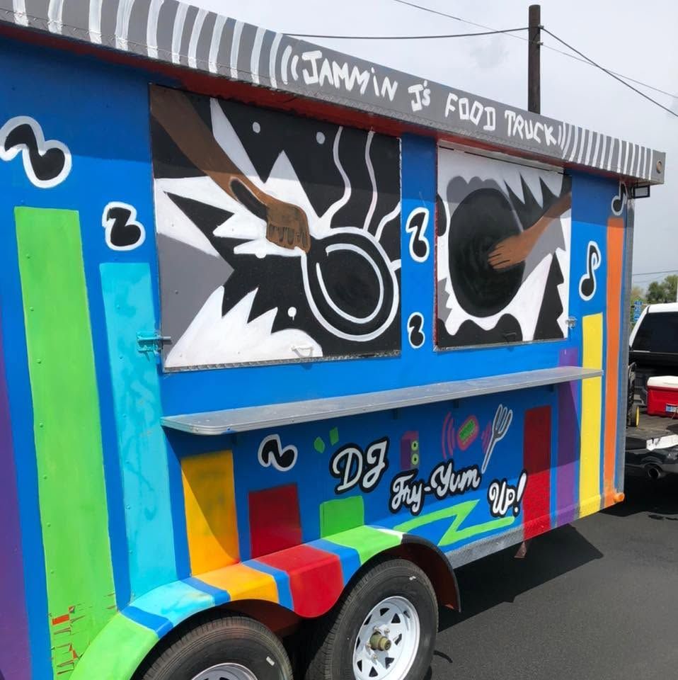 Colorful graffiti-painted food truck with “JAMMIN’ $ FOOD TRUCK” on top, parked outdoors.
