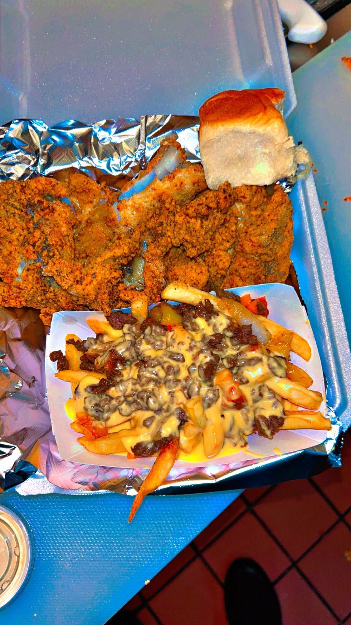 Takeout tray with fried fish, fries, and loaded nachos on a blue table.