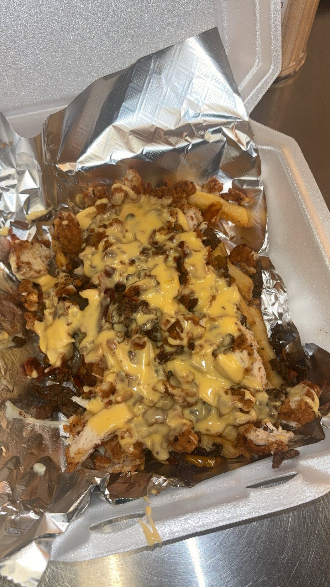 Foil-lined takeout box holding a cheesy, saucy grilled food dish with browned toppings