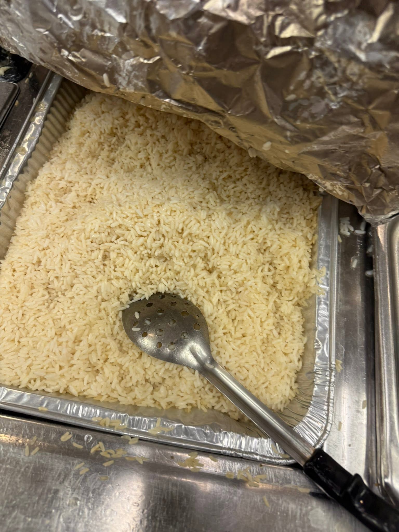 Foil-covered buffet tray with a spoon, holding a light-colored rice or grain dish