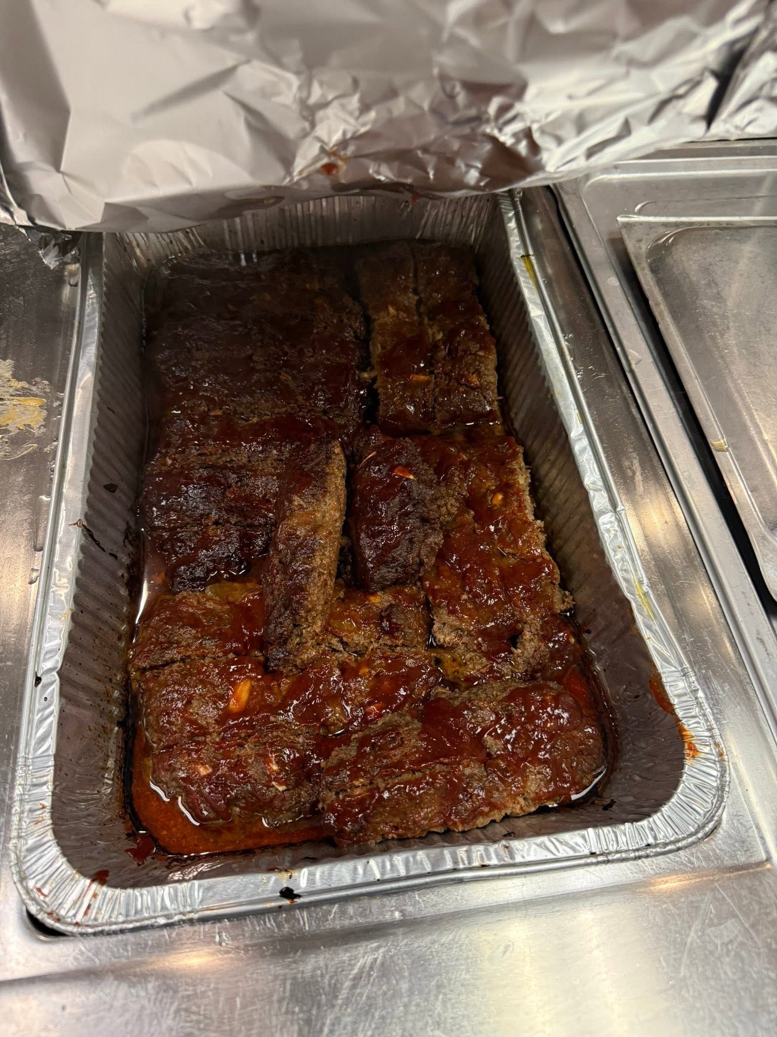 Foil tray of glazed, dark-brown cooked meat in a takeout container