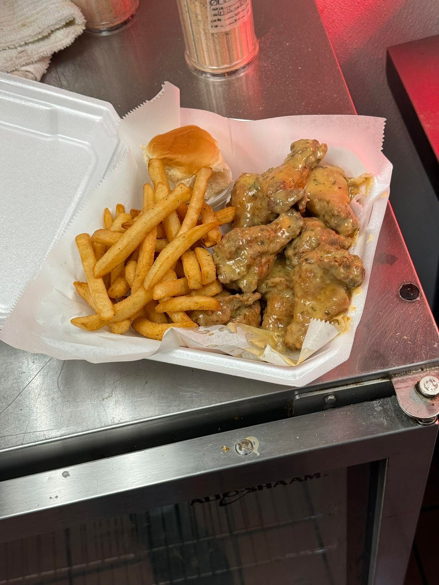Fries and saucy chicken bites in a takeout tray on a metal table