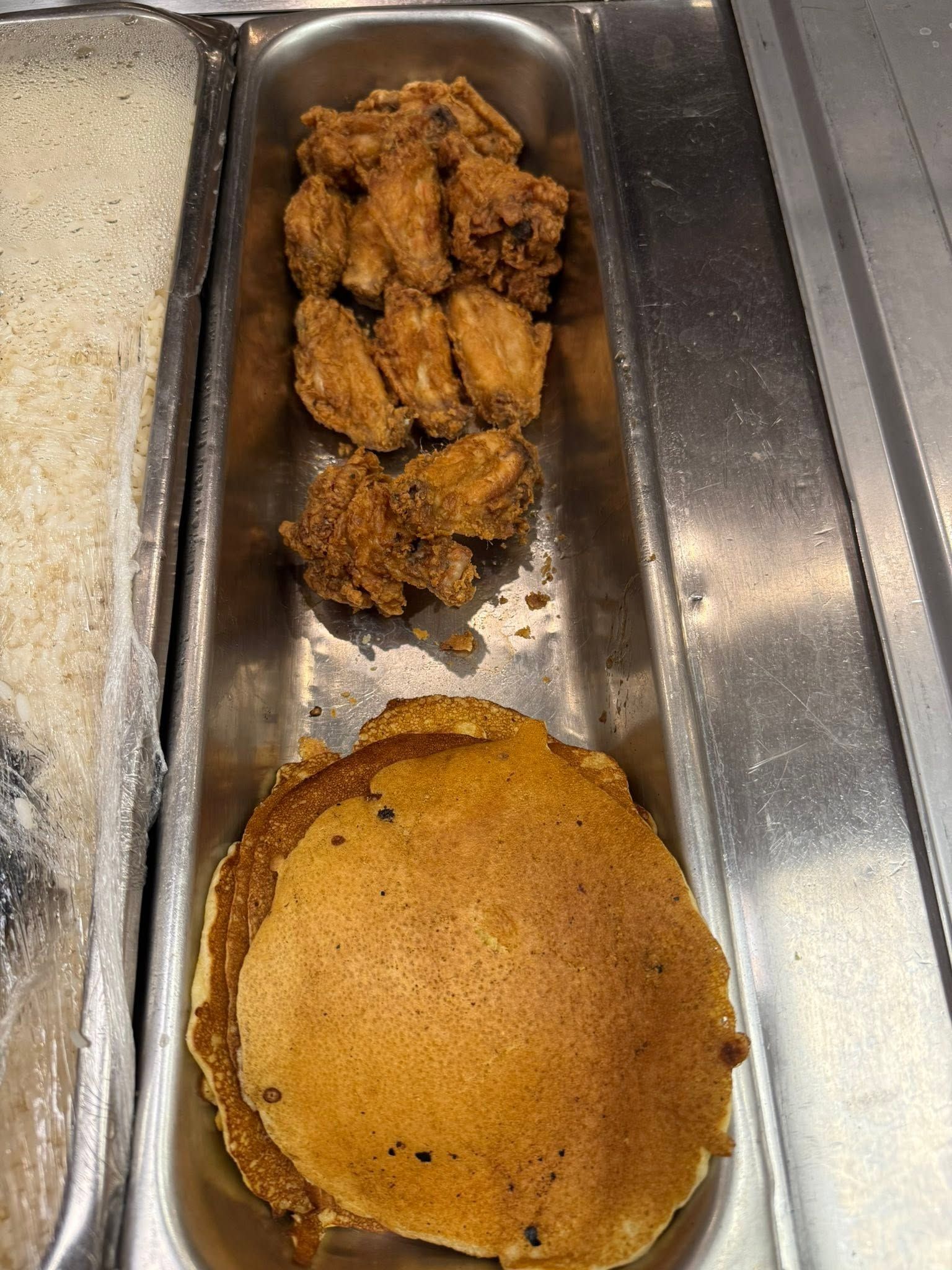 A cafeteria tray with fried chicken wings and a golden pancake.
