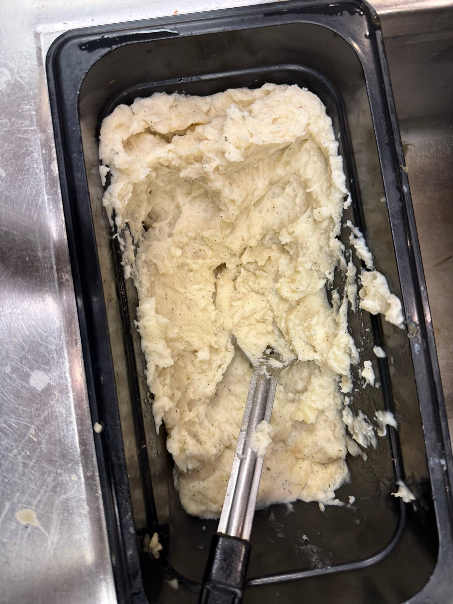 Metal tray with thick mashed potatoes and a serving utensil on a kitchen counter