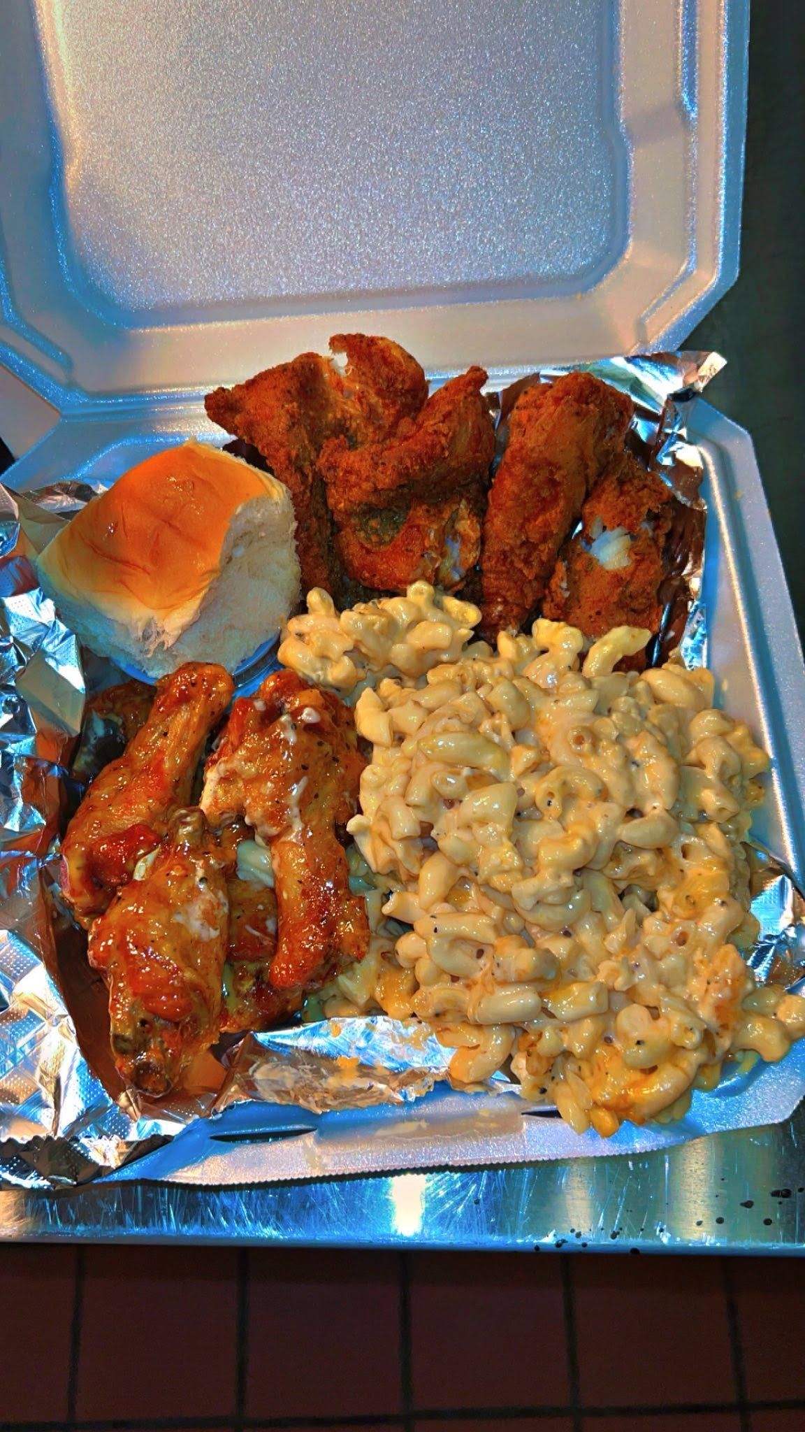 Open takeout container with fried chicken wings, a biscuit, and macaroni and cheese