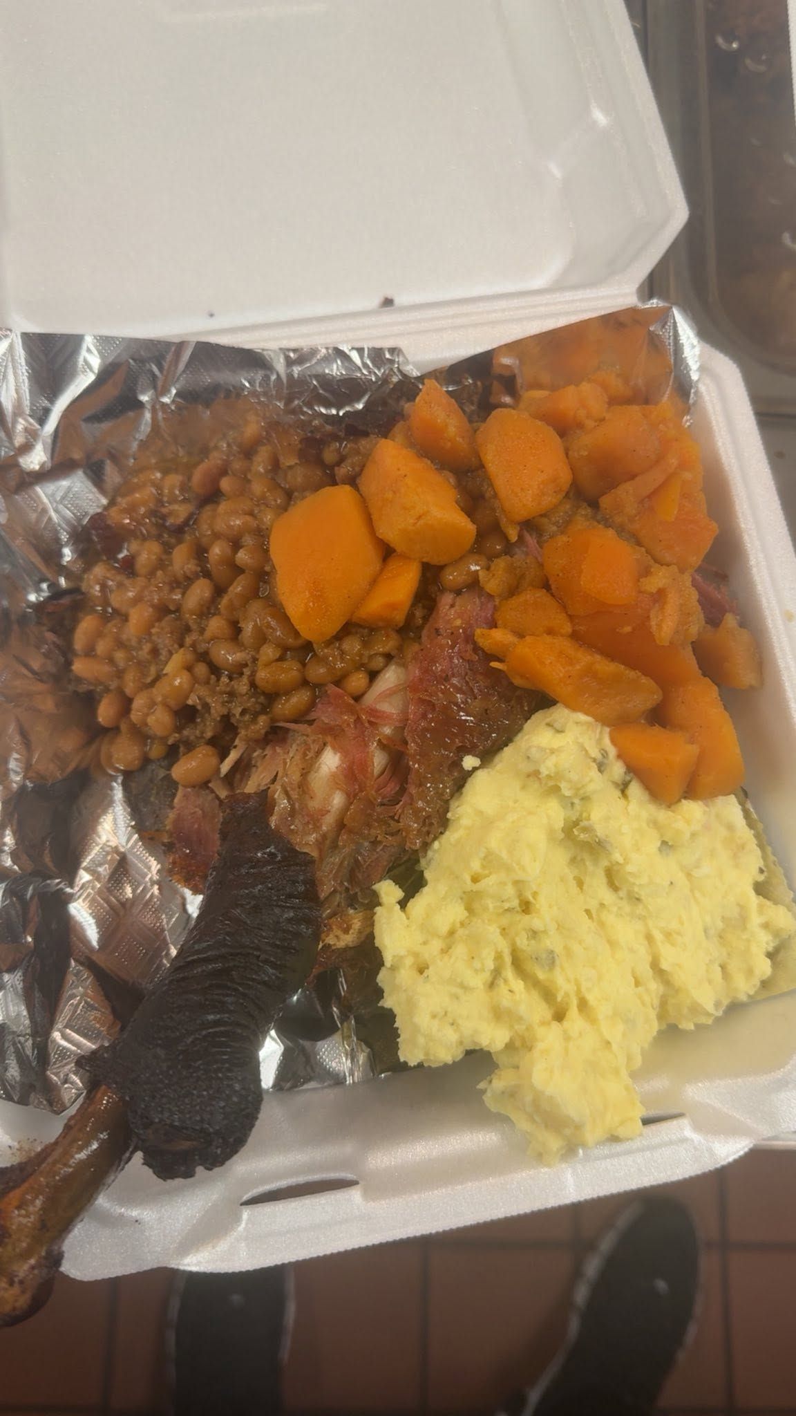 Takeout container with rice, beans, orange vegetables, and meat on a foil-lined tray