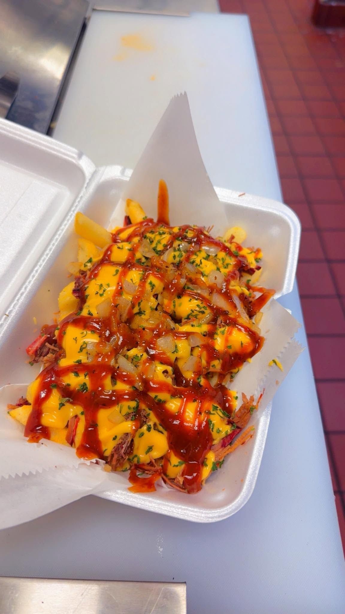 Takeout box of fries topped with melted cheese, sauce, and herbs on a tray