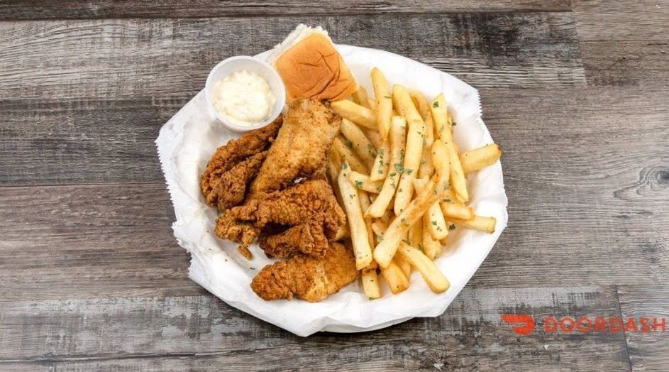 Fried chicken tenders with French fries and dipping sauce on a paper-lined plate