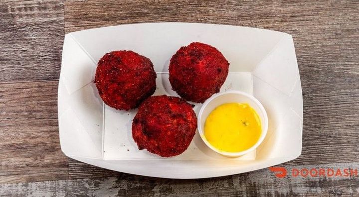 Three red fried snack balls in a white tray with a small cup of yellow dipping sauce
