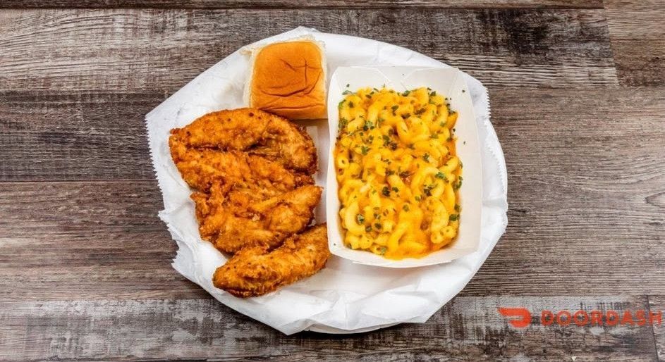 Fried chicken tenders with mashed potatoes and an orange biscuit on a white plate