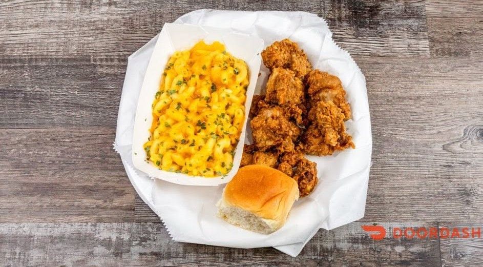 Fried chicken, mac and cheese, and a dinner roll on a white plate over a wooden table