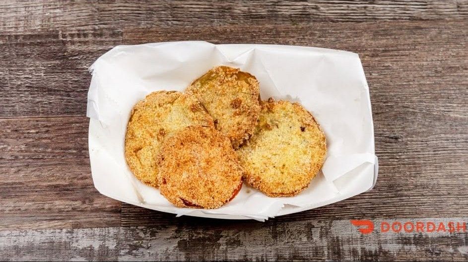 Three breaded, golden-brown patties in a white paper tray on a wooden table