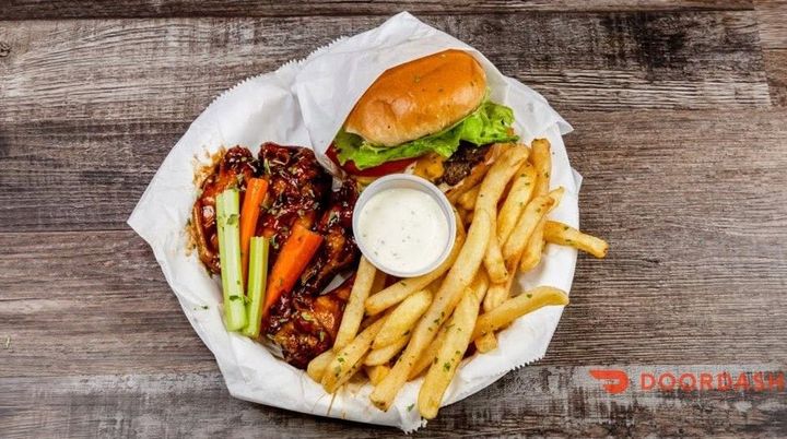 Burger, fries, glazed wings, celery, and dipping sauce on a paper-lined tray.
