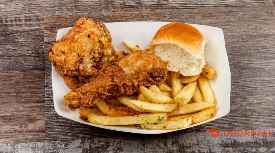Fried chicken tenders, fries, and a bread roll on a white plate on a wooden table.